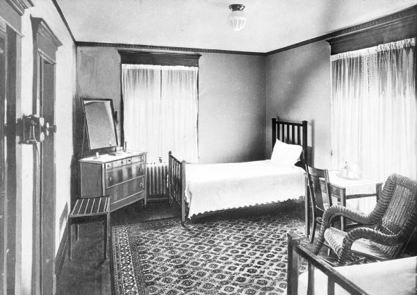 A view of a bedroom at the Fort Bedford Inn. It features two beds, a dresser, mirror, desk, and chairs.