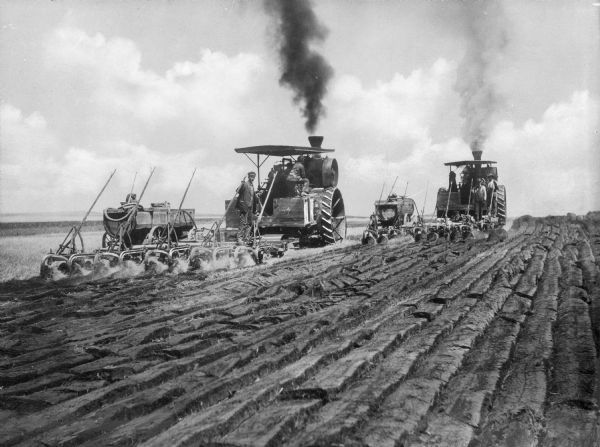 View toward two men on two tractors breaking sod in a field.