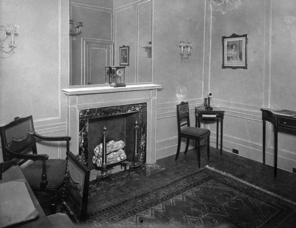 A view of the Ladies' Room at the Washington Trust Co., with a fireplace, mirror, chairs, and other decorations.