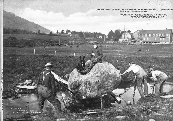 A view of four men and a dog. Caption reads: "Moving the Mayham Memorial Stone into Place. South Gilboa near Stamford, N.Y."