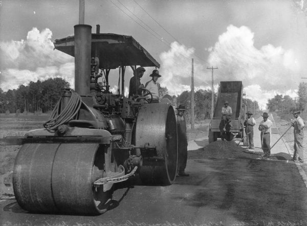 View toward seven men resurfacing a section of Roxboro Road. There is a steam roller in the foreground.
