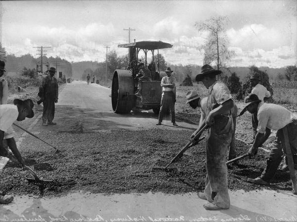 A view of men grating the new surface of Roxboro Road, a section of the U.S. Highway. In the background is a steamroller.