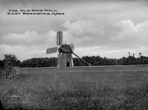 View toward the Old Wind Mill in a field, with a forest in the background. Caption reads: "The Old Wind Mill, East Brewster, Mass."