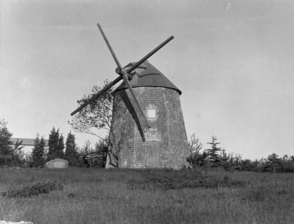 A view of a windmill, with shrubs and trees in the background.