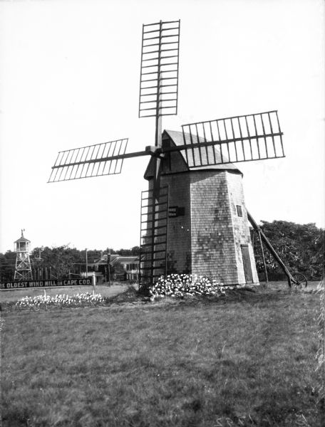 A view of the oldest windmill in Cape Cod, built in 1792. Other buildings and trees are in the background.