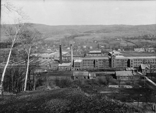 Elevated view from hill toward the Renfrew Mill, built in 1868 and added to the National Historic Register in 1982, a large manufacturing plant with the countryside visible beyond.