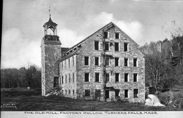 View toward the old mill, an old stone building with a tower and a waterfall behind it. Caption reads: "The Old Mill, Factory Hollow, Turners Falls, Mass."