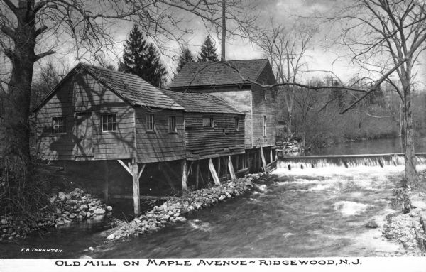 Slightly elevated view toward an old mill on Maple Avenue, next to a pond with a dam. Caption reads: "Old Mill on Maple Avenue -- Ridgewood, N.J."