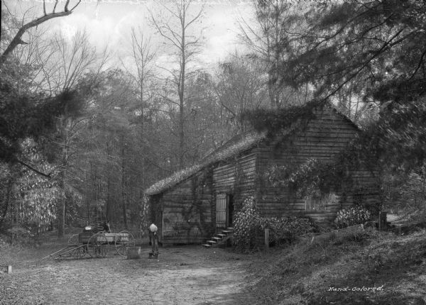 A view of the old mill at the Mill Pond Plantation, with a man standing on a stool with a full bag over his shoulder and a horse and wagon in front of the building.