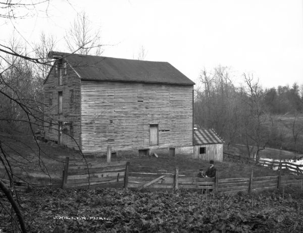 View toward a man and a younger boy posed leaning on a fence in front of an old mill. The mill was built in 1822.