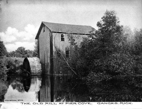 View across water toward the mill. Caption reads: The Old Mill at Pier Cove, Ganges, Michigan."