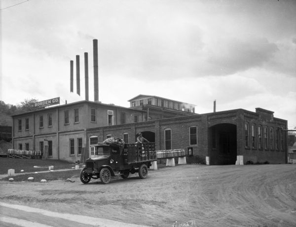 A view of the Borden Co. plant, and a truck parked in front with a man standing in the back.