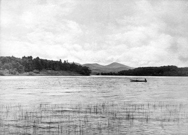 A view of a two people in a boat on Kezar Lake, with the Sabattus Mountains in the distance.