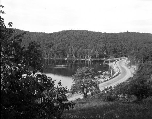 Elevated view of the lake at Bear Mountain Park, with trees in the background and a road bordering one side.