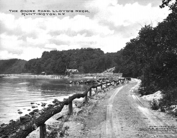 A dirt road along the shore, featuring a log guardrail and a boathouse in the distance. Caption reads: "The Shore Road, Lloyd's Neck, Huntington, N.Y."