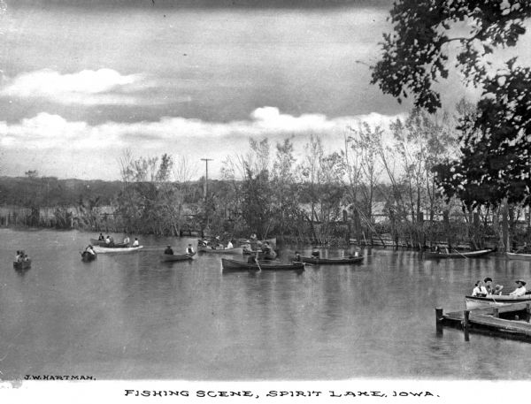 A scene of numerous small boats from which individuals are fishing on Spirit Lake. Caption reads: "Fishing Scene, Spirit Lake, Iowa."