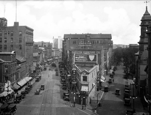 Elevated view of the junction of Congress and First Streets downtown, featuring cars, pedestrians, storefronts, and railroad tracks.