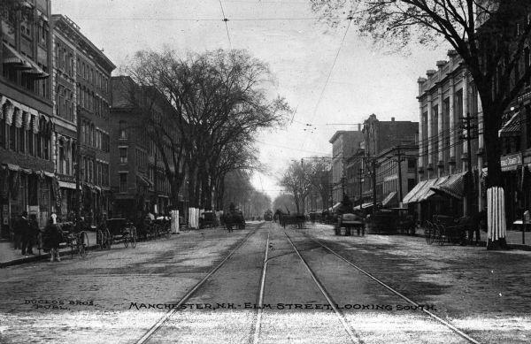 View looking down Elm Street, featuring horse-drawn carriages, pedestrians, buildings, railway tracks, and storefronts. Caption reads: "Manchester, Elm Street, Looking South."