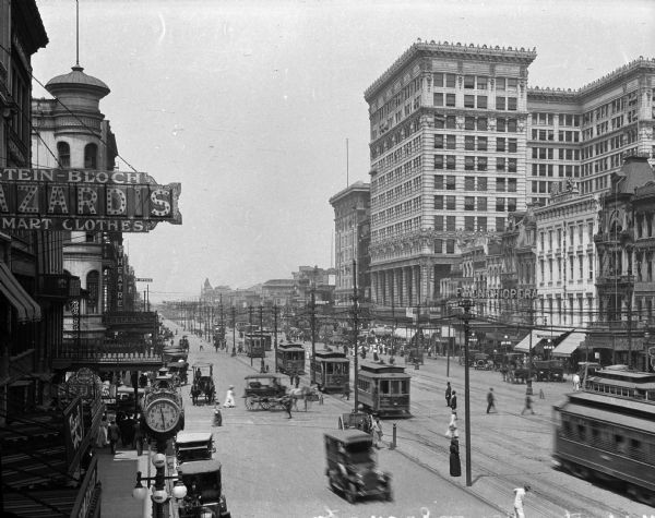 Elevated view looking down Canal Street, featuring cars, pedestrians, trolleys, and a variety of storefronts.