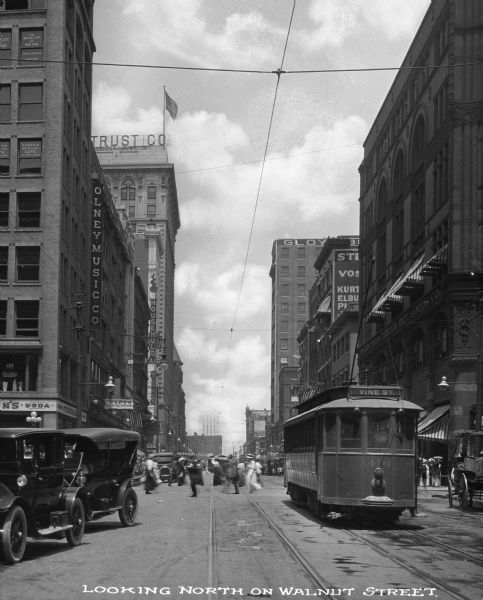 View looking down Walnut Street in downtown which includes a trolley, pedestrians crossing the road, cars, and numerous buildings. Caption reads: "Looking North on Walnut Street."