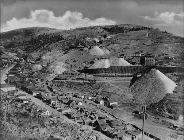 Elevated view of a mining community, including numerous houses, mining structures, and large mounds of gravel material.