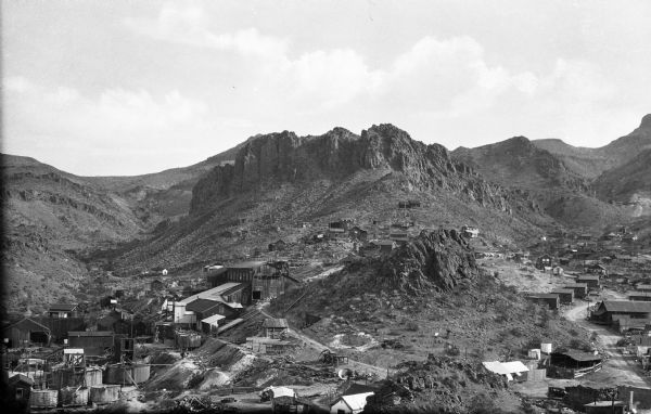Elevated view of mining town in the desert featuring buildings and equipment tucked into the hilly terrain and barren rocky outcroppings.