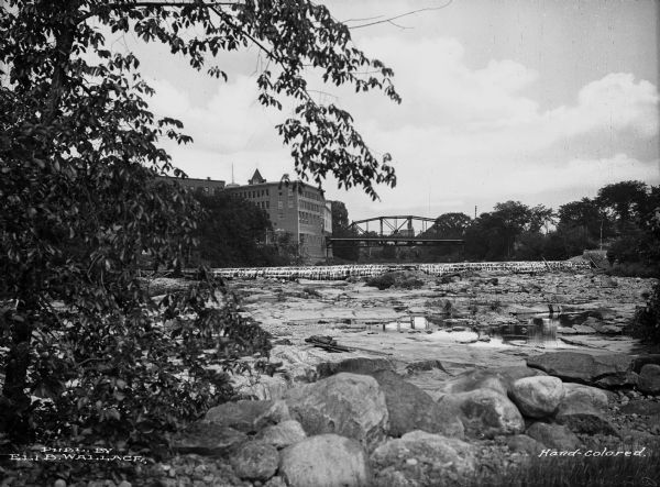 View of river and Ammonoosuc Dam with a bridge and large brick buildings in the background.