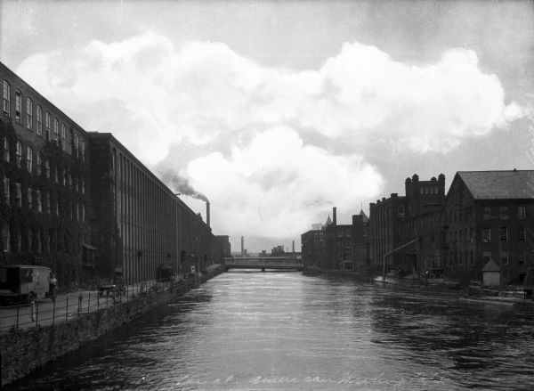 View of the Farmington and Hampshire canal lined with factories and a road. The American Writing Paper Company is on the left.