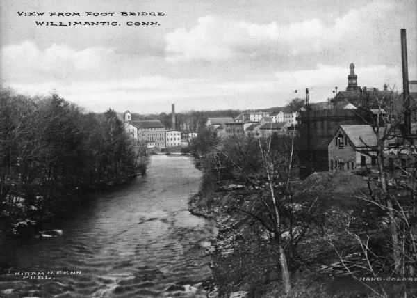 Elevated view of the Willimantic River from a foot bridge with waterfront buildings in the distance. Caption reads: "View from Foot Bridge, Willimantic Conn."