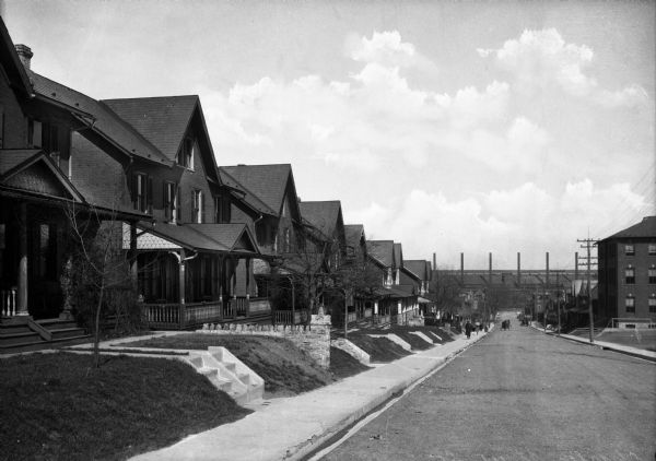 Row of houses on Charles Street with pedestrians, and a steel mill in the distance.
