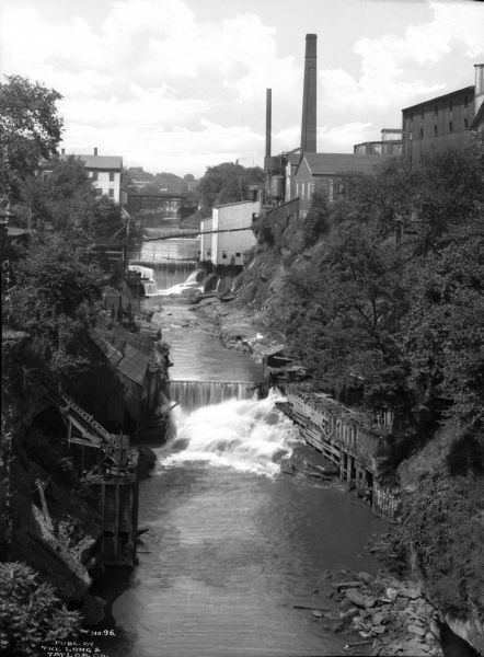 Elevated view of small falls on the Cayahoga River in a gorge with waterfront buildings.