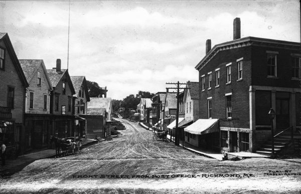 View down Front Street showing businesses and horse-drawn carriages. Caption reads: "Front Street, From Post Office - Richmond, ME."