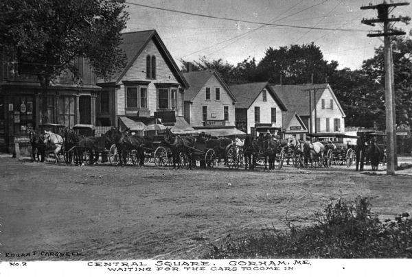 View toward street where horses and buggies are filling the central square, waiting for the arrival of the trolley car. Caption reads: "Central Square, Gorham, ME. Waiting for the cars to come in."