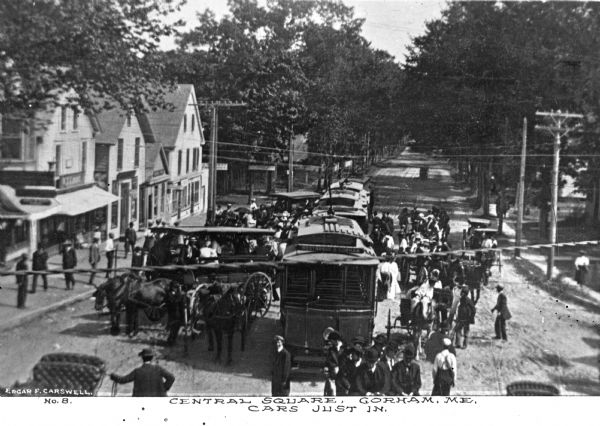 Elevated view of crowds in the central square surrounding arriving trolley cars. Caption reads: "Central Square, Gorham, ME. Cars Just In."