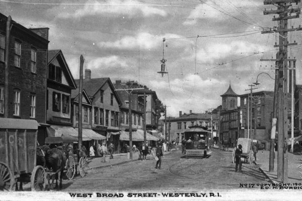 Street side view of West Broad Street including shopfronts, foot traffic, a trolley and horse-drawn wagons. Caption reads: "West Broad Street - Westerly, R.I."