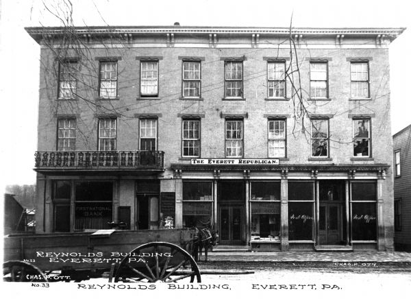 View of the Reynolds building from across the street including a horse-drawn wagon and shopfronts. Caption reads: "Reynolds Building, Everett, PA."