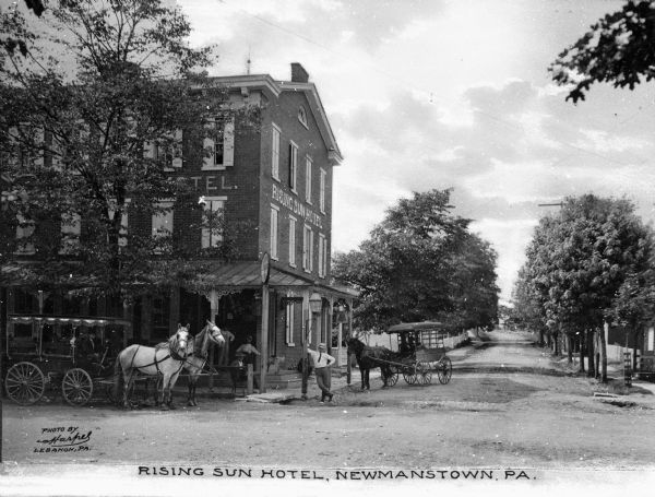 View of the Rising Sun Hotel from across the street. Horse-drawn carriages are parked in front of the hotel while guests relax on the porch. Caption reads: "Rising Sun Hotel, Newmanstown, PA."
