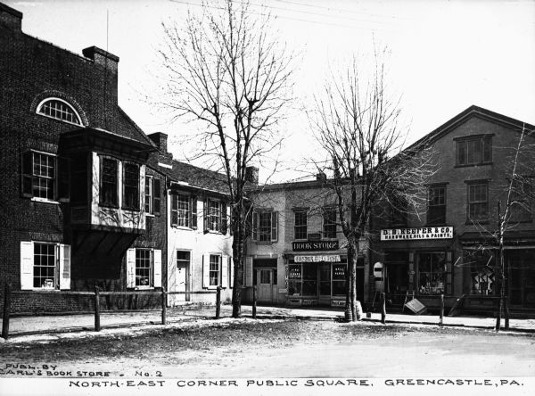 The North East corner of public square. Features connected buildings which house a book store and a hardware store. Caption reads: "North-East Corner Public Square, Greencastle, PA."