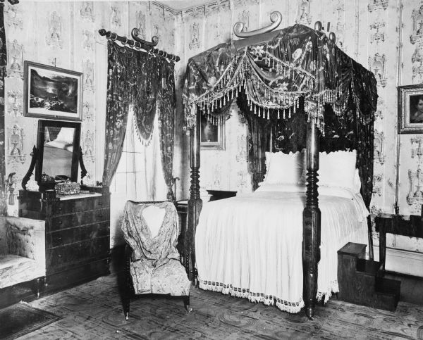 Interior view of a bedroom at the Hermitage, home of Andrew Jackson, featuring a canopied bed, matching curtains, ornate wallpaper and gleaming carved wooden furnishings.