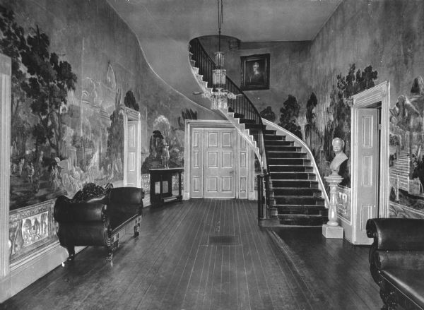 Foyer of the Hermitage, home of Andrew Jackson, featuring bucolic murals, a curving staircase, ornate couches and sculptures.
