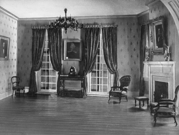 Parlor in the home of James K. Polk. The relatively empty room contains three carved chairs, a few paintings, a chest and two ornate ceramic pitchers.
