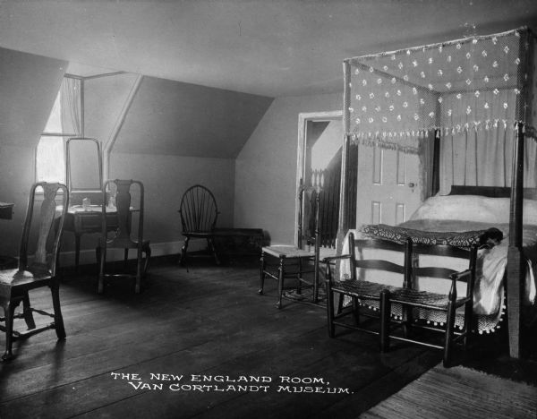 Interior view of the New England bedroom in the Van Cortlandt house. Features a bed with an embroidered translucent canopy, several chairs, and a vanity set near the window. Caption reads: "The New England Room, Van Cortlandt Museum."
