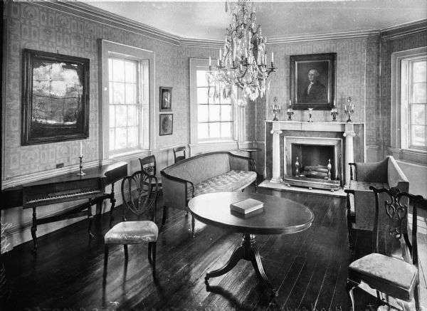Interior view of the Morris-Jumel Mansion which served, at different times, as headquarters to both forces during the Revolutionary war.  This view of the meeting room features elegant carved wooden furniture, a harpsichord, chandelier and a fireplace framed by carved columns. A portrait of George Washington hangs above the fireplace and other paintings line the walls.