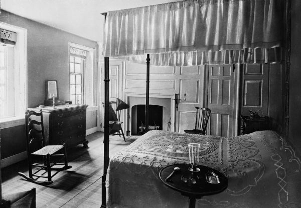 General, and later president, George Washington's bedroom. Features room with a dresser, chairs, fireplace, and a canopied bed with side table.