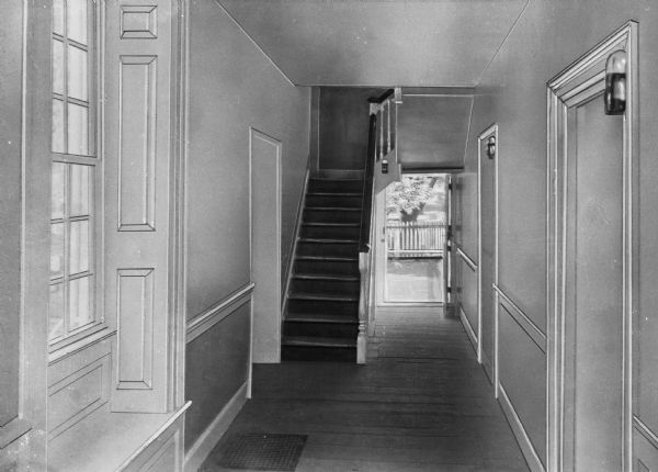 Hallway in George Washington's headquarters showing a staircase, a window with a built in seat, several doors along the wall on the right, and sun streaming in from a balcony in the background.