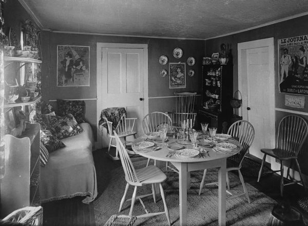 View of small dining room, with a table set for dinner. The walls are decorated with posters and ceramics are on display throughout the room.