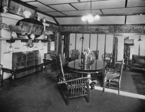 Interior view of a dining room featuring table with a small sculpture in the center, rustic chairs, a screened in fireplace, decorative vases, flower arrangements and paintings.