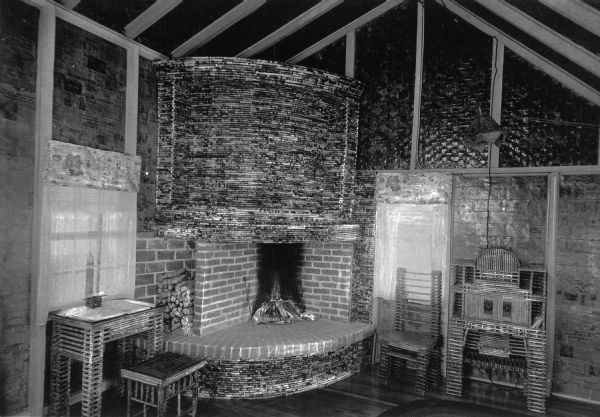 Interior view of the Paper House, featuring furniture and fireplace embellishments constructed out of rolls of newspaper. The walls and windows are also decorated with paper.