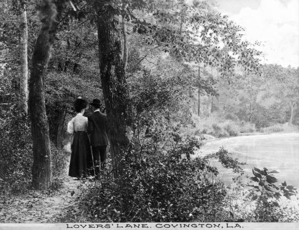 A couple walking down a wooded lakeside path. The caption reads: "Lovers' Lane, Covington, LA."