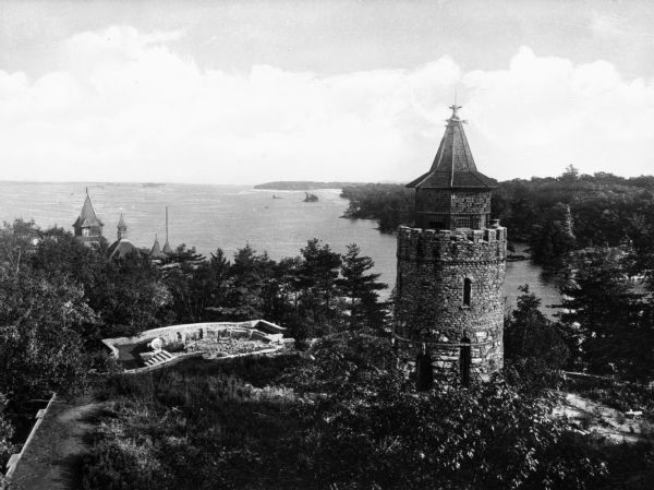 Elevated view of a round stone tower and a small stone courtyard on the bay in the Thousand Islands.